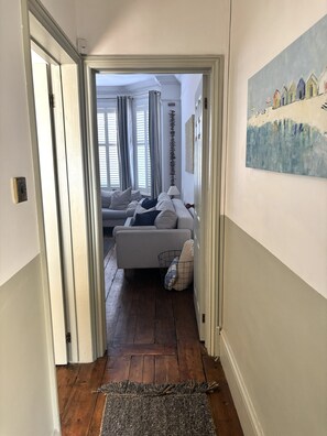 Ein Flur, der in ein Wohnzimmer mit einer Couch, einem Gemälde an der Wand und einem Holzboden führt.