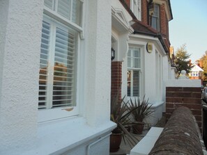 A white house with a brick wall, a small garden with potted plants, and a white fence.
