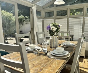 A conservatory with a dining table set for four, surrounded by white chairs, with a vase of flowers on the table. - Shipside Village Location
Calm & relaxing Eastbourne apartment & private garden (Eastbourne)