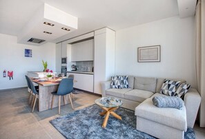 A modern living room with a sofa, a coffee table, and a dining area with chairs and a table.