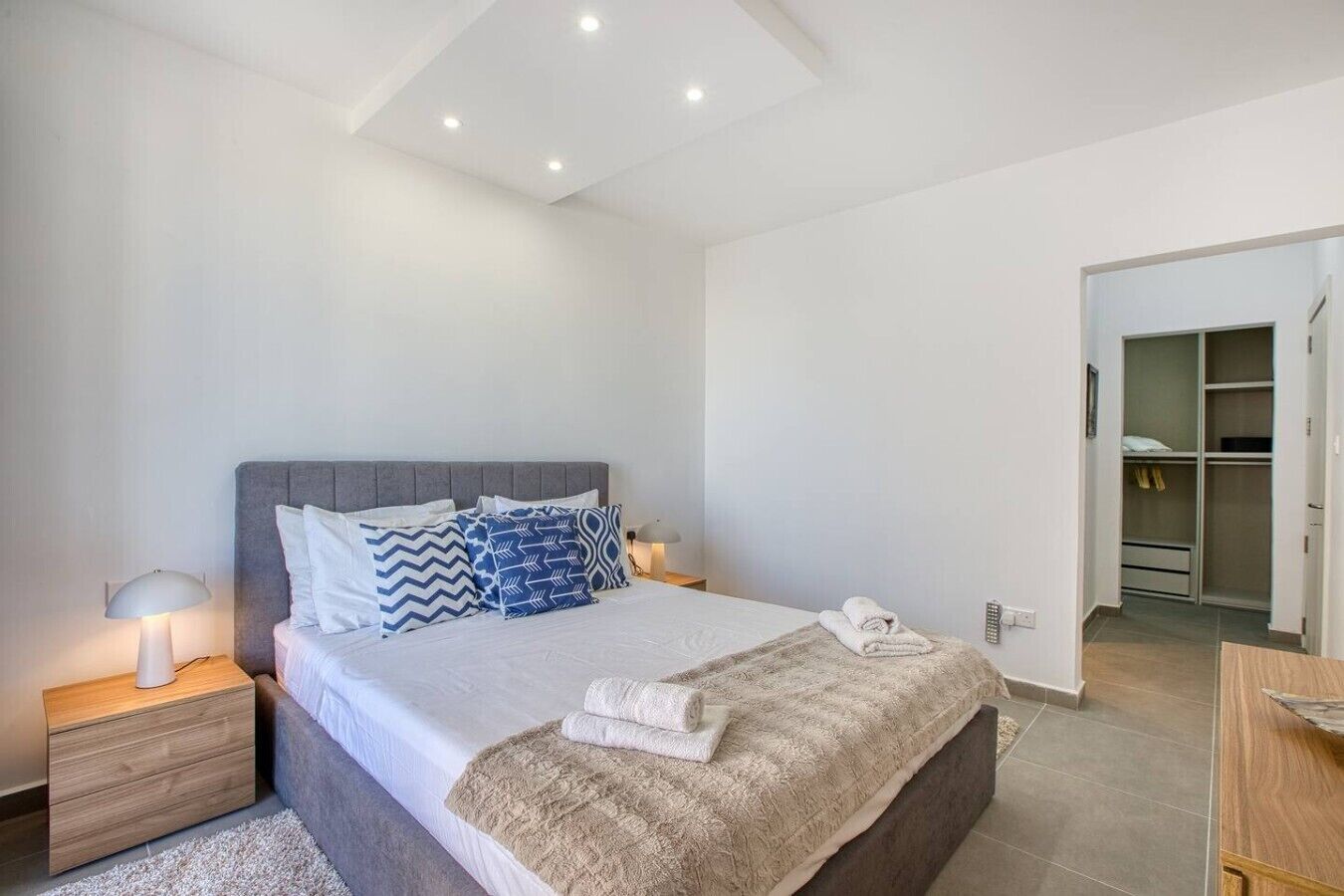 Une chambre à coucher moderne comprenant un lit, des tables de chevet, une commode, une lampe, un placard et une salle de bain.