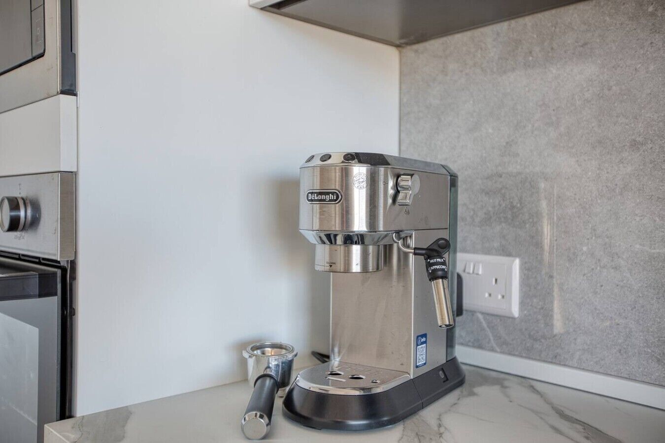 Une machine à expresso De'Longhi dotée d'un mousseur à lait, d'un moulin à café et d'un distributeur d'eau, le tout posé sur un plan de travail en marbre.