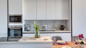 Cozinha moderna com eletrodomésticos embutidos, área de jantar com bancada de mármore e uma pequena planta em vaso.