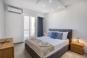Un dormitori modern amb un llit gran, una tauleta de nit, una làmpada de nit i vistes a l'exterior a través d'una porta corredissa.