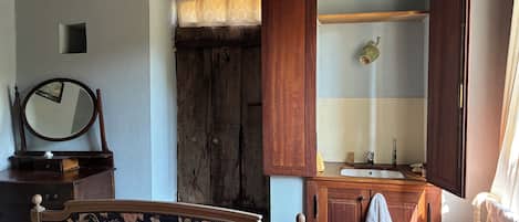 A bedroom with a bed, a wooden wardrobe, a mirror, and a window with curtains.