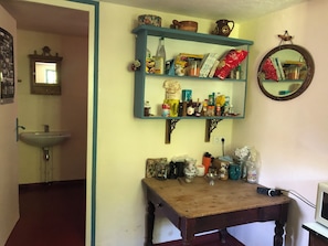 A kitchen with a sink, a wooden table, and shelves stocked with various food items and kitchenware.