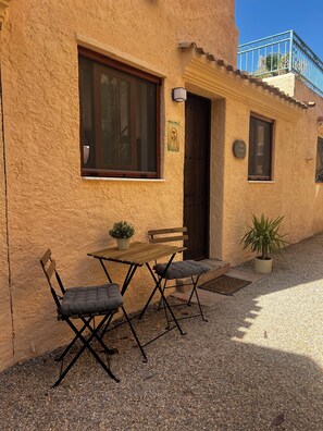 A building with a textured facade, a wooden door, a window with a dark frame, a small balcony with a metal railing, and a potted plant. - Casa Alba in Sierra Cabrera, recently renovated with the most amazing views. (Cortijo Cabrera)