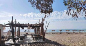 Ein Außenbereich mit Tischen, Stühlen, einer Holzpergola und Strandstühlen.