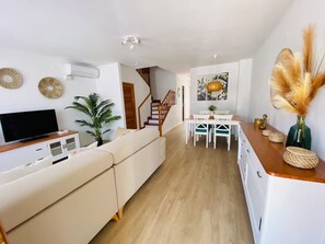 Ein modernes Wohnzimmer mit einem Flachbildfernseher, einer Couch, einem Essbereich mit Tisch und Stühlen sowie einer Treppe, die in eine weitere Ebene führt.