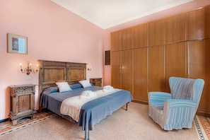 Ein Schlafzimmer mit einem großen Bett, einem Holzschrank, einem gestreiften Sessel und einem kleinen Nachttisch mit Lampe.