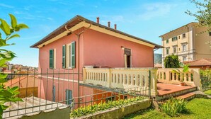Una villa rosa con balcón, rodeada por una cerca blanca y follaje.