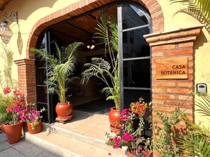 A building entrance with a sign reading 'CASA BOTANICA,' surrounded by potted plants and flowers. - Casa Botanica (Lo de Marcos)