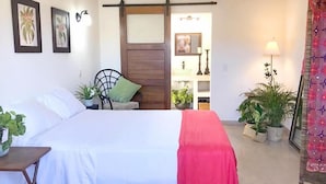 A bedroom with a bed, a chair, and a table. There are potted plants and a lamp. - Casa Botanica (Lo de Marcos)
