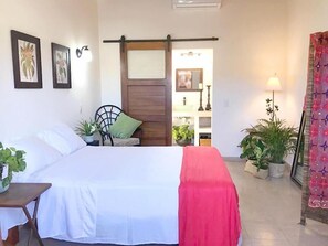 A bedroom with a bed, a chair, and a table. There are potted plants and a lamp. - Casa Botanica (Lo de Marcos)