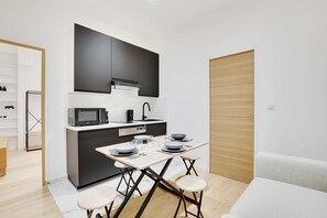 A compact kitchen with modern appliances, a dining table with four stools, and a wooden door. - Cosy Modern Flat 1BR 4P Oberkampf (Paris)