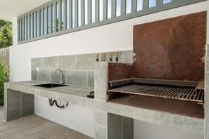 An outdoor kitchen with a built-in grill, a sink, and a window above the grill. - Born | 2Bed Pool View | Up to 6 Guests (Bavaro)