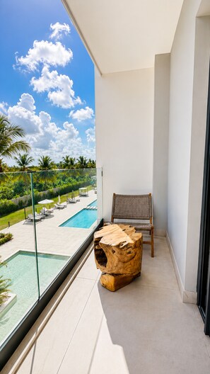 A balcony with a view of a swimming pool, a wooden stool, and a chair. - Born | 2Bed Pool View | Up to 6 Guests (Bavaro)