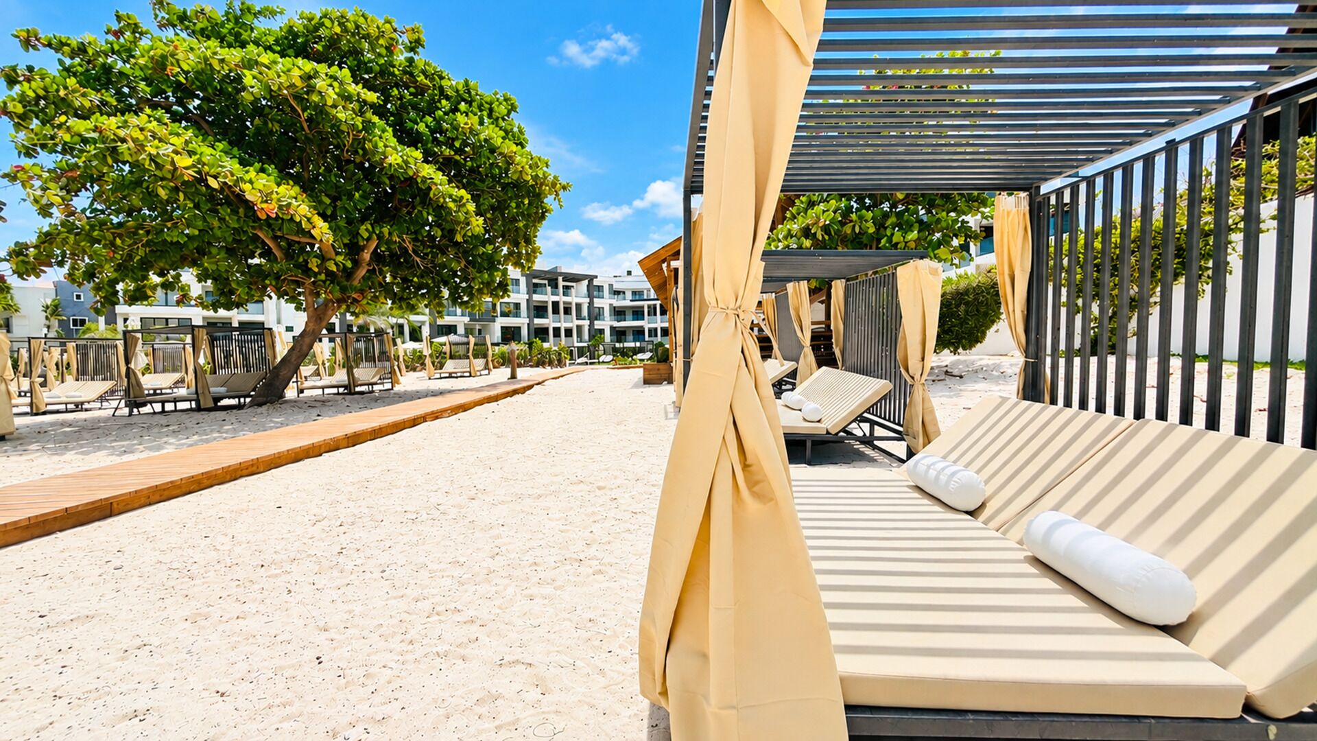 Een terras aan het strand met ligbedden, een houten dek en een overdekte zithoek.