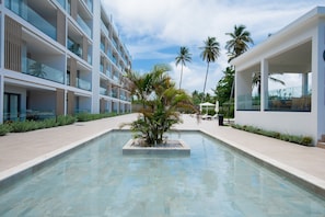 A modern hotel with a pool, palm trees, and a clear sky. - Born | 2Bed Pool View | Up to 6 Guests (Bavaro)