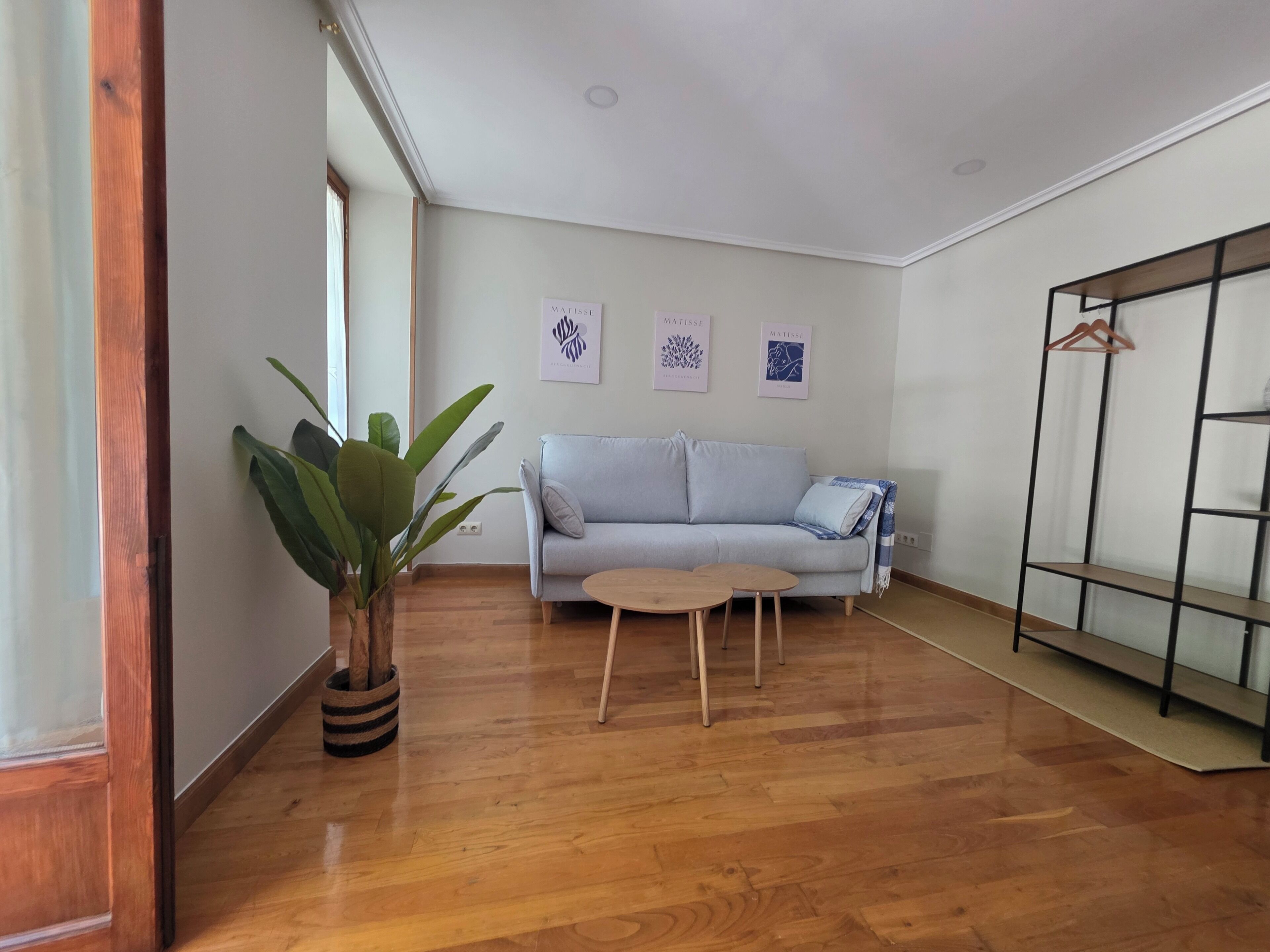 Un salon comprenant un canapé, deux petites tables, une plante en pot et une étagère en métal.