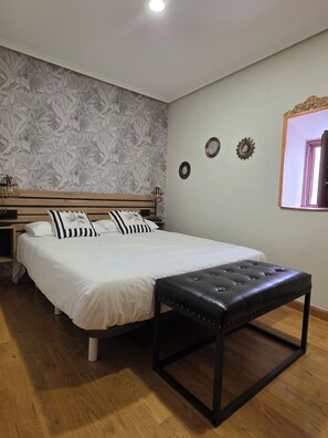 A bedroom with a bed, a wooden bench, a nightstand, and a wall with decorative items. - Beautiful, bright apartment in the port of Ferrol (Ferrol)