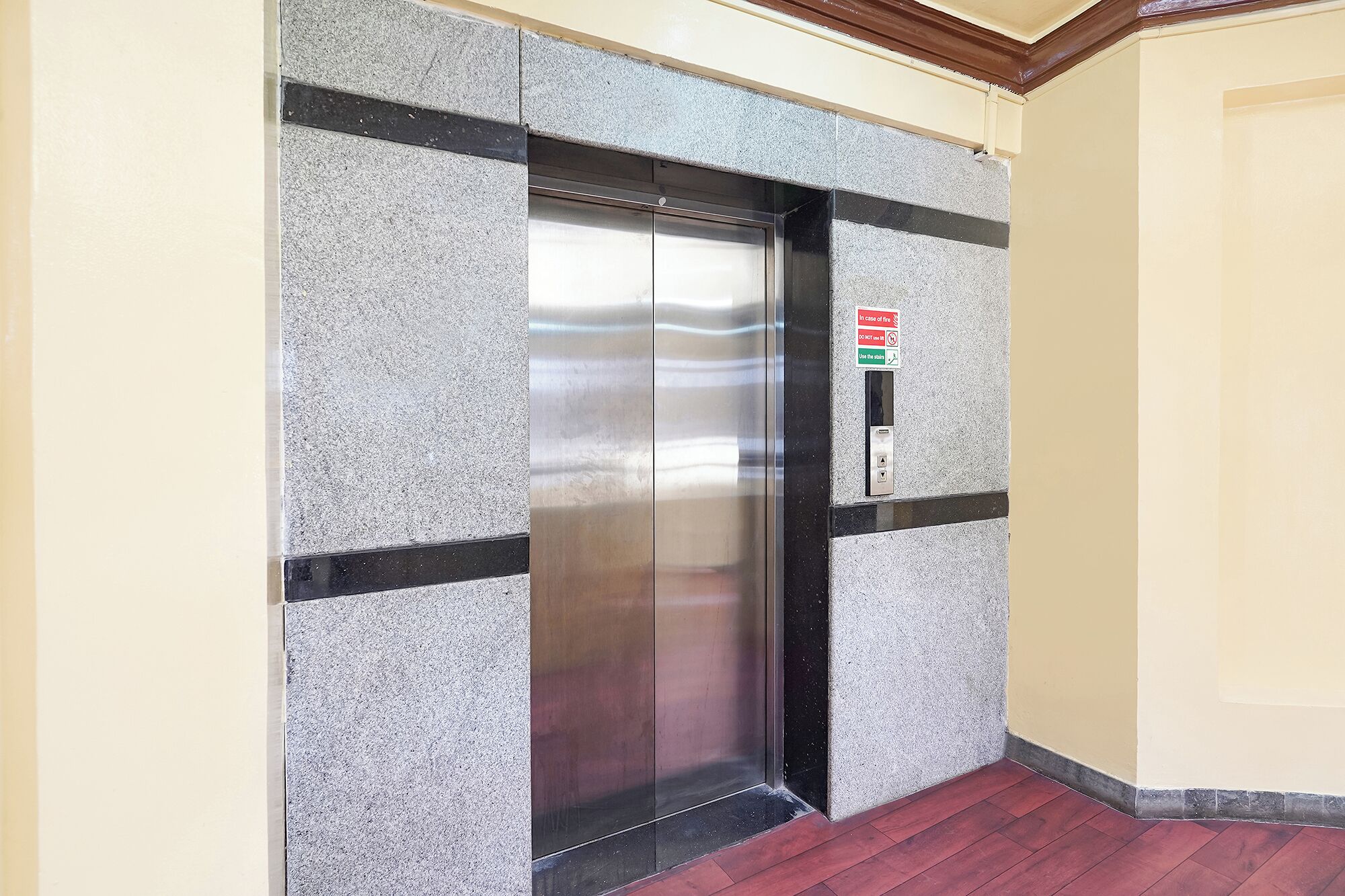 An elevator with a metallic finish, a fire safety sign, and a red-tiled floor.