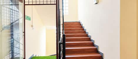 Una escalera que lleva al primer piso, con una puerta de cristal a la izquierda y una alfombra verde en la base.