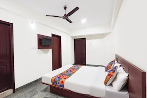 Un dormitorio con una cama, un ventilador de techo y un televisor montado en la pared.