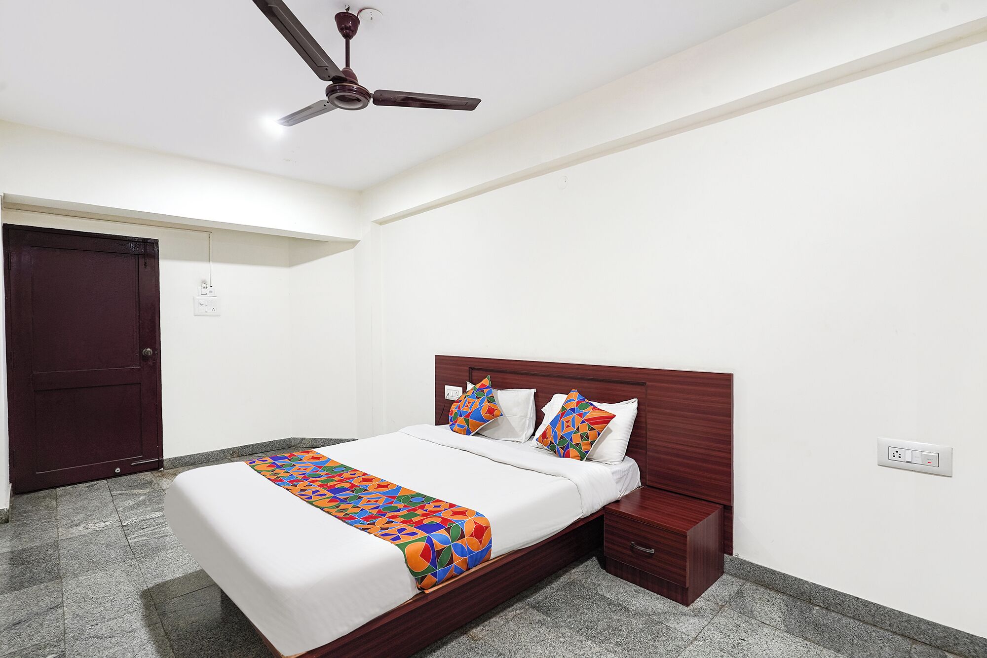 A bedroom with a bed, nightstand, wooden headboard, ceiling fan, and a door.