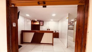 Zona de recepción con mostrador de madera, suelo de baldosas blancas y un pequeño mostrador con fotografías enmarcadas.