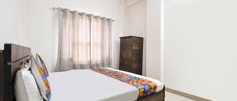 A bedroom with a bed, curtains, a wardrobe, and a window.