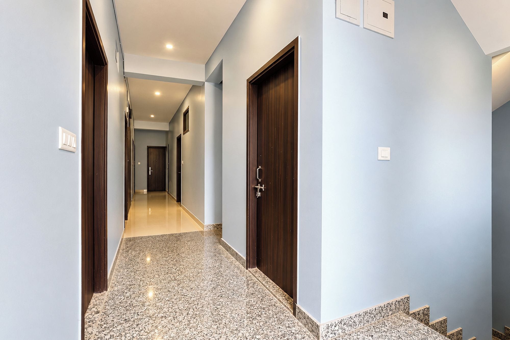 Un couloir avec un plancher ciré, une porte en bois et un interrupteur sur le mur.