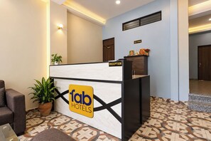 A reception desk with a sign for 'fab hotels', a potted plant, and a reception area with a patterned floor.