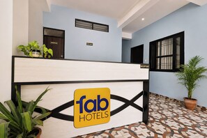 Ein Hotelrezeptionstresen mit einem Schild für 'fab hotels'. Auf dem Tresen stehen Blumentöpfe und darüber befindet sich ein Empfangsschild.