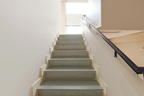 Una escalera con barandilla que sube hacia una zona luminosa en la parte superior.