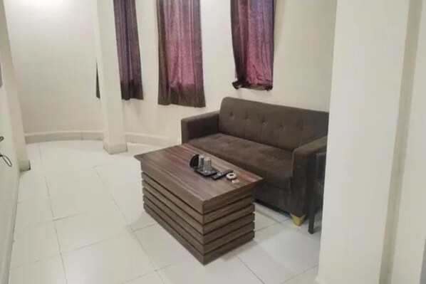 Una sala de estar con un sofá marrón, una mesa de centro de madera y una ventana con cortinas moradas.