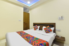 A hotel room with a bed, a nightstand, a wall socket, and a ceiling light. - Fabhotel Jmd 11 (Indore)
