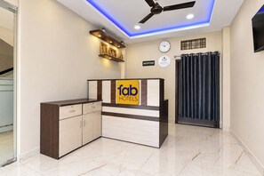 A hotel reception desk with a sign for 'fab hotels,' a ceiling fan, a clock, and a reception sign. - Fabhotel Jmd 11 (Indore)