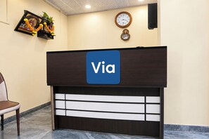 A reception desk with a 'Via' sign, a clock, and a framed picture with flowers on the wall.