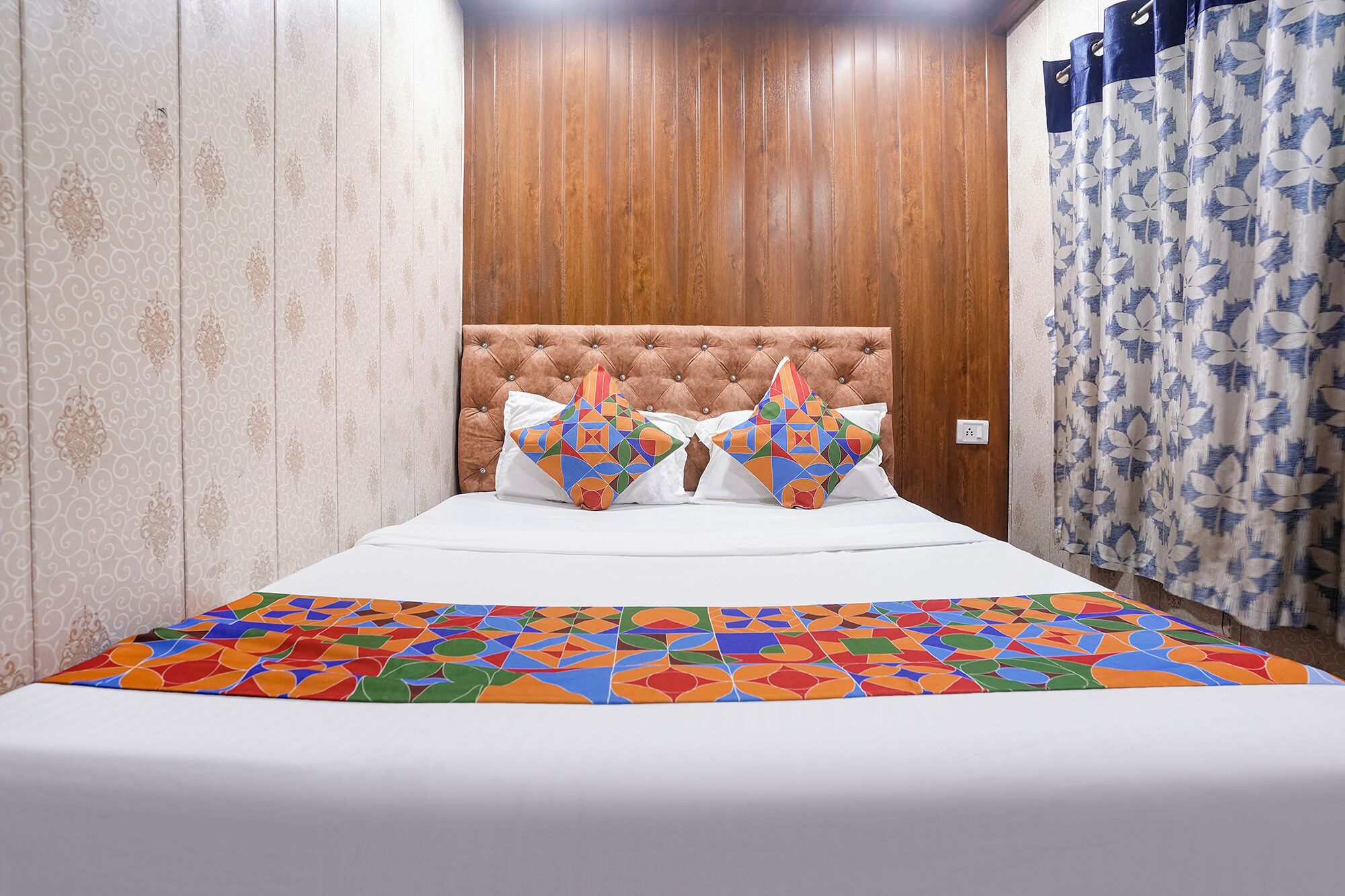A bed with a geometric-patterned bedspread, a tufted headboard, and two decorative pillows.