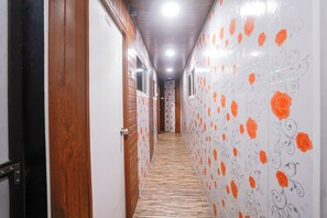 A hallway with wooden flooring, white walls with orange floral patterns, and a door on the left.