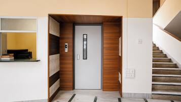A modern interior with a wooden door, a digital lock, a staircase, and a wall-mounted shelf with books.