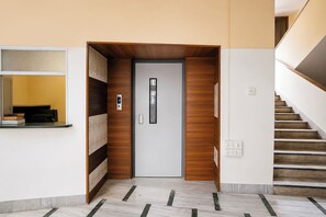 A modern interior with a wooden door, a digital lock, a staircase, and a wall-mounted shelf with books. - Via Shiv Vandana Inn (Mumbai)