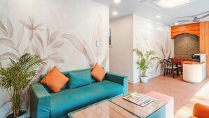Un moderno vestíbulo de hotel con un sofá color turquesa, cojines naranja y una mesa de centro de vidrio, además de un mostrador de recepción.