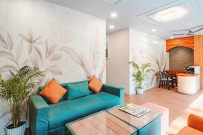 Eine moderne Hotelhalle mit einem türkisfarbenen Sofa, orangefarbenen Kissen, einem Glastisch und einer Rezeption.