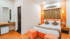 Habitación de hotel con cama, escritorio con espejo, cafetera, equipo de aire acondicionado y piso de madera.