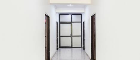 A hallway with a tiled floor, a door with a glass panel, and a ceiling with recessed lighting.