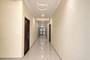 A hotel corridor with a marble floor, a wooden door with a number plate, and a modern ceiling light fixture. - Fabhotel Grg Bhawan (Vrindavan)