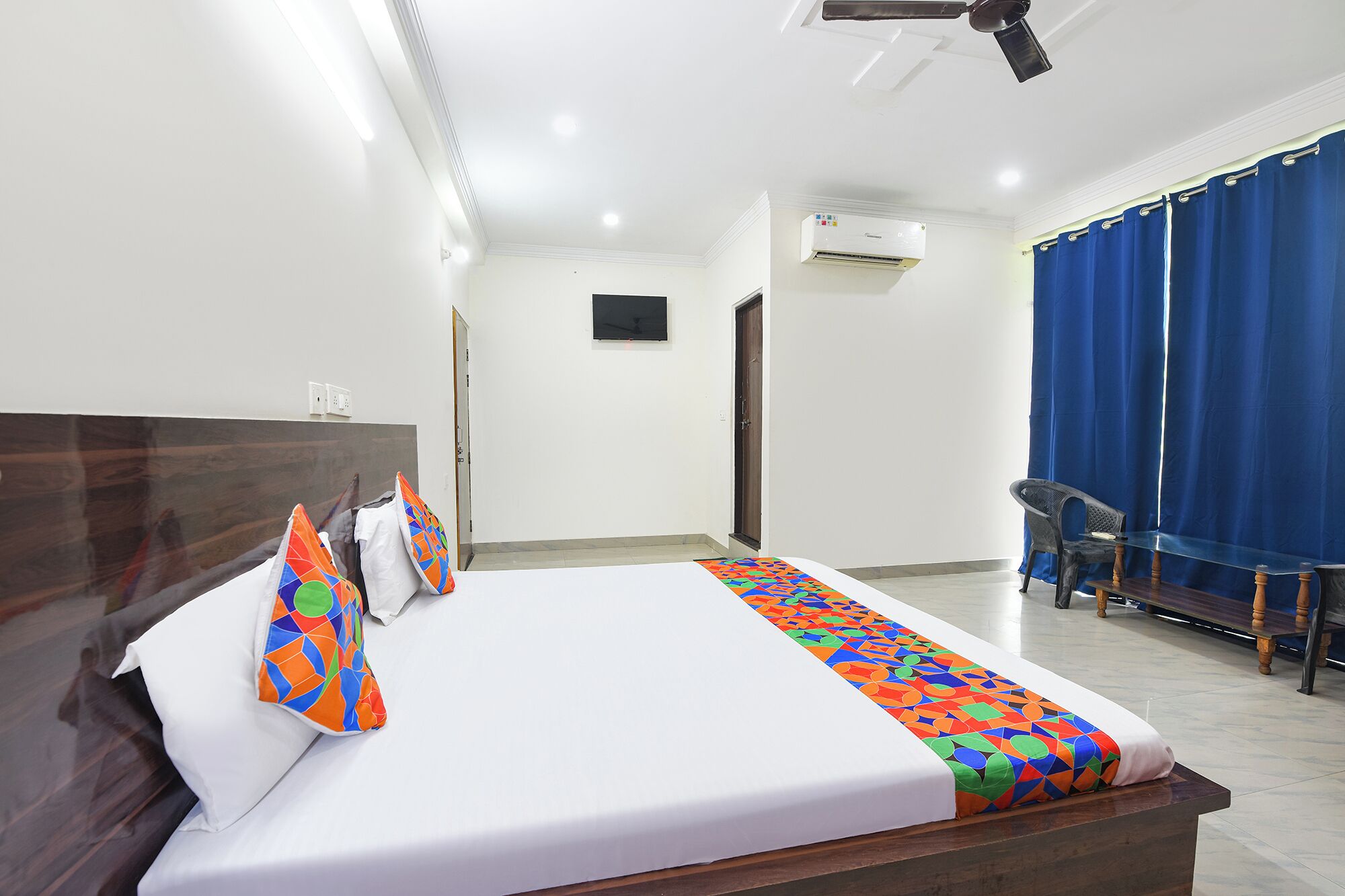 Habitación de hotel con cama, escritorio, silla, ventana con cortinas y unidad de aire acondicionado.