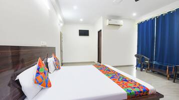 Habitación de hotel con cama, escritorio, silla, ventana con cortinas y unidad de aire acondicionado.